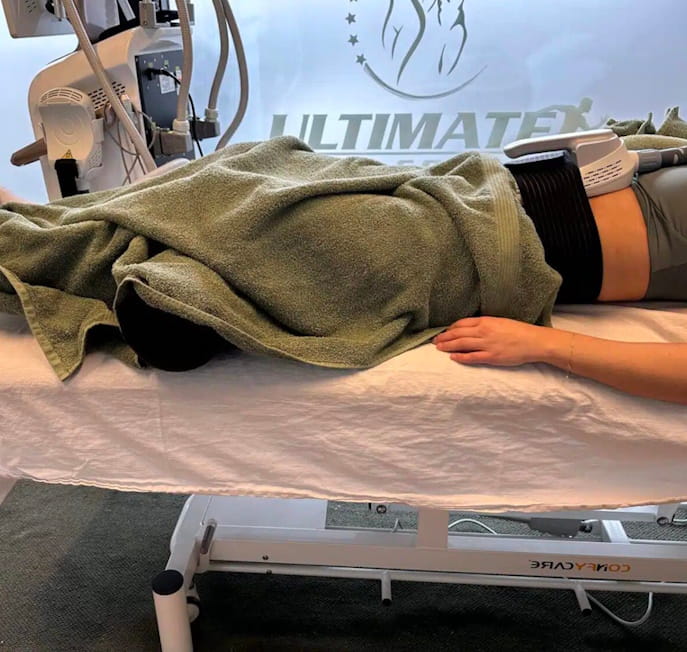 Kvinde ligger på briks med håndklæder over sig og modtager e- body sculpting